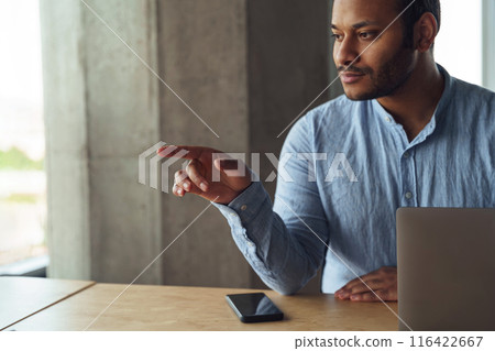 A man sits at a table with a laptop, pointing at something 116422667