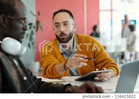 Colleagues Discussing Ideas Using Tablet and Laptop in Office 116423822