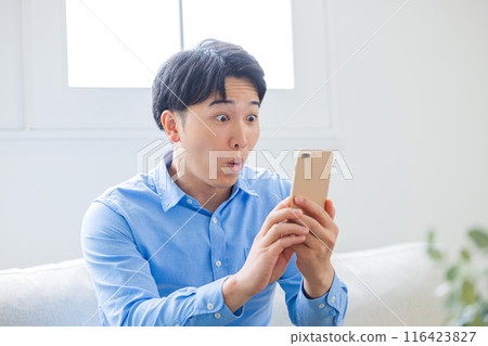 A young man surprised while looking at his smartphone 116423827