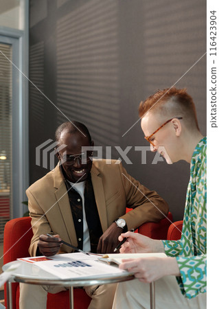 Coworkers Reviewing Documents Together in Office 116423904