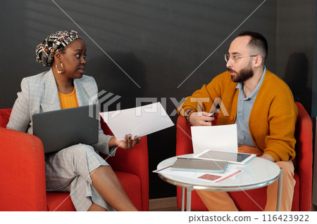 Colleagues Discussing Documents in Office Lounge 116423922