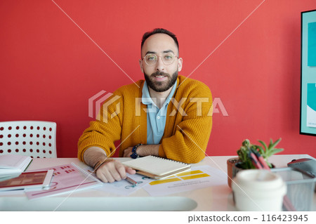 Portrait of Man Sitting at Desk in Modern Office with Red Wall Portrait of Man Sitting at Desk in Modern Office with Red Wall 116423945