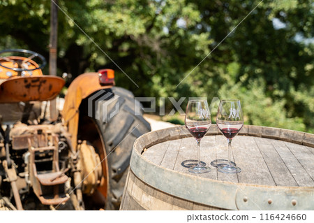 Charming Rustic Vineyard Winery with Wine Glasses on Barrel near Vintage Tractor 116424660
