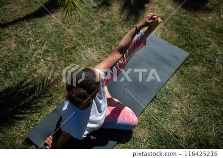 Top view of woman practicing yoga outdoors on grass mat, wearing colorful leggings 116425216