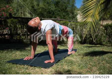 Woman practicing yoga outdoors on a sunny day in a serene garden setting Woman practicing yoga outdoors on a sunny day in a serene garden setting 116425229