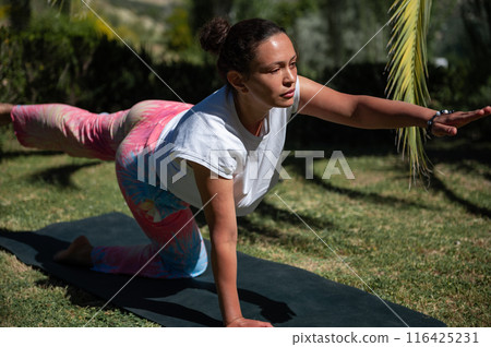 Woman practicing yoga outdoors in a garden, performing balancing exercise on yoga mat Woman practicing yoga outdoors in a garden, performing balancing exercise on yoga mat 116425231