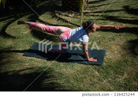 Woman practicing yoga outdoors on mat in colorful leggings on a sunny day Woman practicing yoga outdoors on mat in colorful leggings on a sunny day 116425244