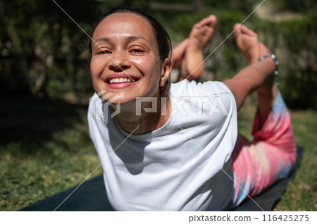 Smiling woman practicing yoga outdoors on sunny day with focus on fitness and well-being 116425275