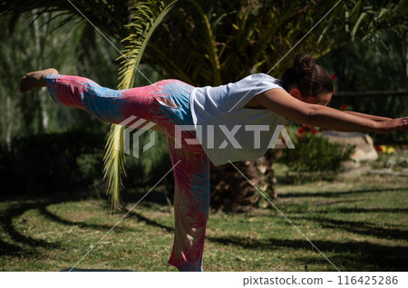 Woman practicing yoga outdoors in warrior three pose at a serene park Woman practicing yoga outdoors in warrior three pose at a serene park 116425286