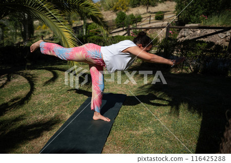 Woman practicing yoga outdoors in warrior pose on a sunny day in nature 116425288