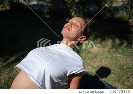 Woman practicing yoga outdoors in sunlight, performing upward-facing dog pose 116425320