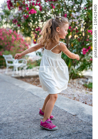 Portrait of little girl in white dress happy smiling on blooming park background in Croatia 116425400
