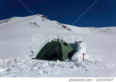 Lone tent pitched on snowy Mount Elbrus slope, surrounded by icy peaks. Green tent amid white snow, adventure travel, extreme camping at high altitude. 116425887