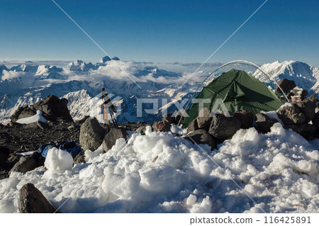 Solo traveler camp on Mount Elbrus summit. Lone tent in snow, rocks, extreme mountain backdrop. Adventurous climber gear on rugged terrain, with breathtaking views. 116425891