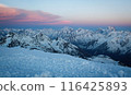 Sunset hues bathe Caucasus Range, peaks covered in snow. Orange and pink sky above frosty mountain tops. Alpine landscape at dusk, serene nature view. 116425893