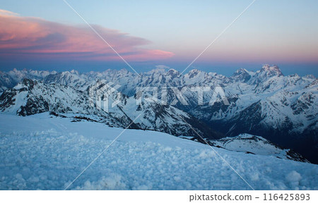 Sunset hues bathe Caucasus Range, peaks covered in snow. Orange and pink sky above frosty mountain tops. Alpine landscape at dusk, serene nature view. Sunset hues bathe Caucasus Range, peaks covered in snow. Orange and pink sky above frosty mountain tops. Alpine landscape at dusk, serene nature view. 116425893