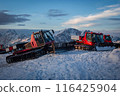 Snowcats parked on snowy Elbrus mountains during sunset. Red and pink vehicles prepare ski slopes, cold and rugged terrain. Winter adventure, maintenance in remote icy landscape. 116425904