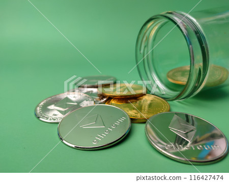 Glass jar with silver ethereum and golden bitcoin digital crypto coin on green background 116427474