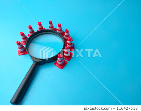 Mini plastic cones and magnifying glass on a blue background with copy and text space. Mini plastic cones and magnifying glass on a blue background with copy and text space. 116427518