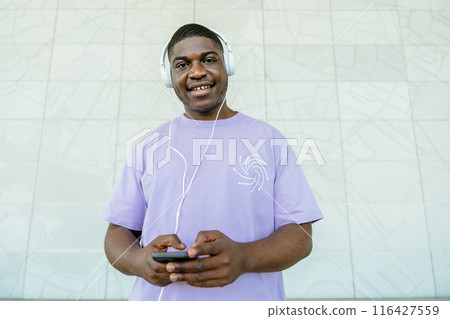 African man with headphones, reding text messages on his smartphone, looking at camera. African man with headphones, reding text messages on his smartphone, looking at camera. 116427559