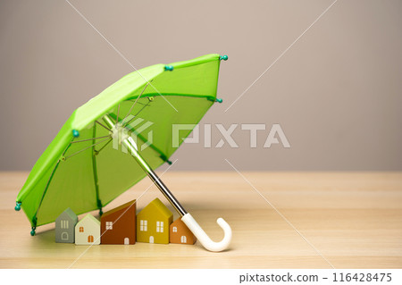 Property and home insurance concept. Wooden houses stand under a green umbrella. Financial security. Repairs or rebuilding in the event of a covered loss. 116428475