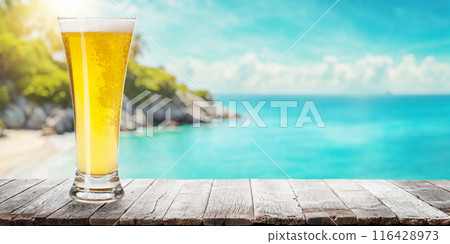Glass of beer on a table with a stunning sea and beach background 116428973