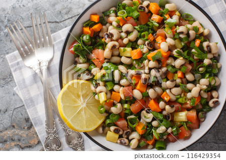 Winter salad with black-eyed beans, carrots, onions, tomatoes, basil, parsley dressed with olive oil closeup on the plate. Horizontal top view Winter salad with black-eyed beans, carrots, onions, tomatoes, basil, parsley dressed with olive oil closeup on the plate. Horizontal top view 116429354
