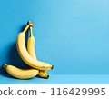 Cluster of ripe bananas is neatly arranged on a vibrant blue background, creating a striking contrast. The bananas are yellow with brown spots, indicating their ripeness. 116429995