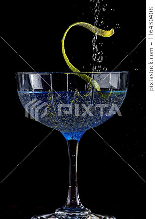 Blue cocktail being prepared with a splash of liquid and lemon twist garnish 116430408