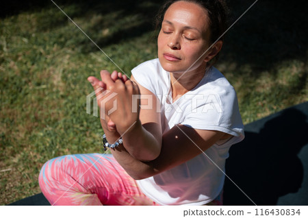 Woman practicing yoga outdoors on a sunny day, meditating with eyes closed in serene environment 116430834