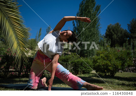 Woman practicing yoga outdoors on a sunny day, stretching and doing poses in a serene and peaceful garden 116430848