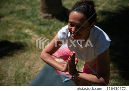 Smiling woman practicing yoga outdoors in a sunny park 116430872