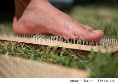 Close-up of bare foot stepping on a bed of nails, outdoors on grass 116430880