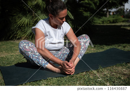 Woman practicing yoga outdoors on a sunny day, seated on a mat in a meditative pose Woman practicing yoga outdoors on a sunny day, seated on a mat in a meditative pose 116430887