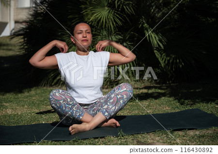 Woman practicing yoga outdoors on a sunny day, meditating and stretching on a yoga mat in a serene garden setting Woman practicing yoga outdoors on a sunny day, meditating and stretching on a yoga mat in a serene garden setting 116430892