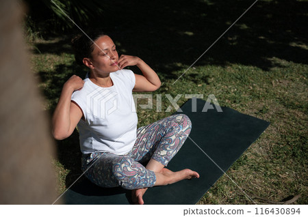 Woman meditating outdoors on a yoga mat in the sunshine, practicing mindfulness and relaxation in nature 116430894