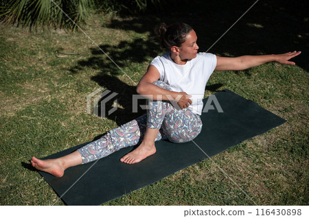 Woman practicing yoga outdoors on a sunny day, stretching on a mat in a peaceful park Woman practicing yoga outdoors on a sunny day, stretching on a mat in a peaceful park 116430898