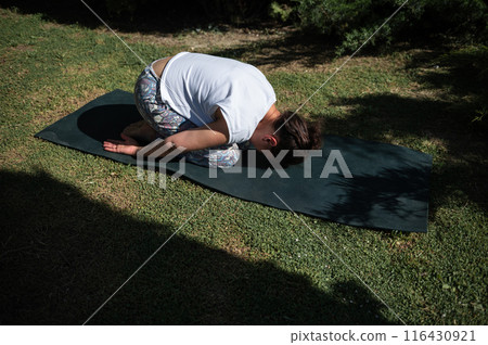 Woman practicing child pose yoga outdoors on a sunny day Woman practicing child pose yoga outdoors on a sunny day 116430921