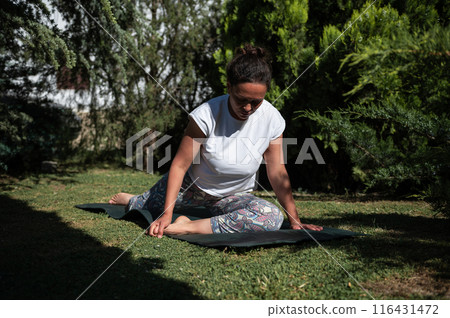 Woman practicing yoga in a serene garden setting on a sunny day 116431472