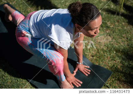 Woman practicing outdoor yoga exercise on a mat in a park 116431473