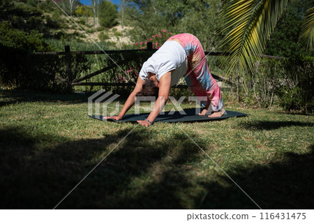 Woman practicing yoga outdoors in downward dog pose on grassy field under the sun 116431475