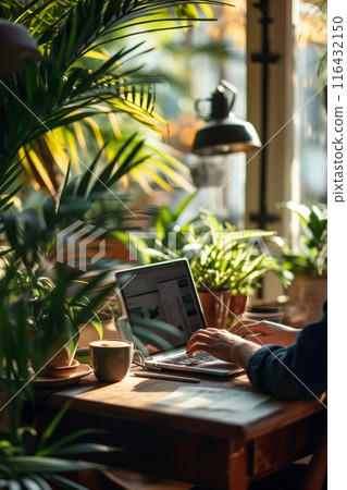 Warm indoor setting with a person working on a laptop surrounded by lush houseplants and a cup of coffee. 116432150