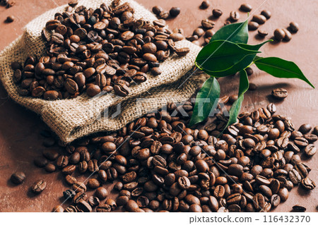 Burlap bag scattering coffee beans with green leaves on table. Top view, flat lay 116432370