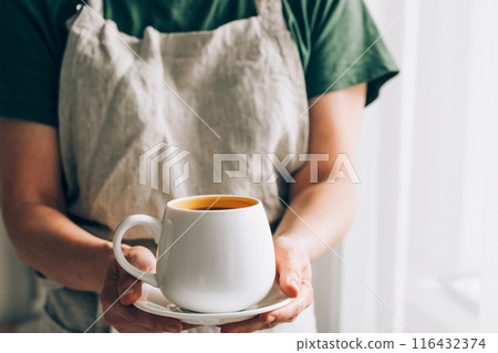 A Barista man or waiter in a linen apron serves white cup of coffee on a saucer. Hot drink in hands 116432374