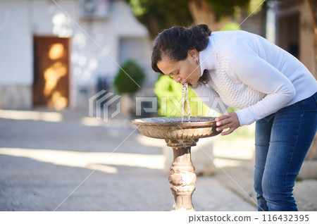 Woman drinking water from an outdoor public fountain Woman drinking water from an outdoor public fountain 116432395