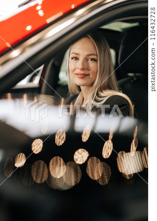 Vertical portrait of happy female buyer choosing new car in showroom automobile salon looking at camera, touch wheel, make decision buy. Smiling woman driver enjoy sitting in luxury transport vehicle. Vertical portrait of happy female buyer choosing new car in showroom automobile salon looking at camera, touch wheel, make decision buy. Smiling woman driver enjoy sitting in luxury transport vehicle. 116432728