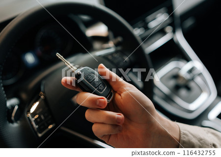 Close-up cropped shot of unrecognizable driver male holding key to new car in hand. Closeup view of happy man sitting in drivers seat behind steering wheel in car. Concept of smart key car technology. Close-up cropped shot of unrecognizable driver male holding key to new car in hand. Closeup view of happy man sitting in drivers seat behind steering wheel in car. Concept of smart key car technology. 116432755