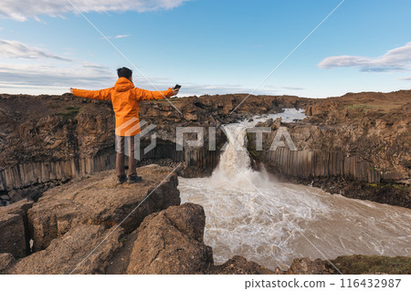 Traveler man enjoying with Aldeyjarfoss waterfall flowing among the Icelandic Highland in summer at Iceland Traveler man enjoying with Aldeyjarfoss waterfall flowing among the Icelandic Highland in summer at Iceland 116432987