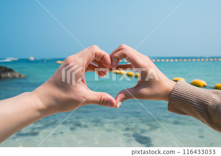 Couple two hands forming and making heart shape gesture on the beach 116433033