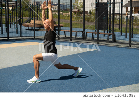 Athlete handsome male make fitness exercises and stretch on courtyard sports ground. Workouts and morning routines. Public sports field at modern city. Athlete handsome male make fitness exercises and stretch on courtyard sports ground. Workouts and morning routines. Public sports field at modern city. 116433082